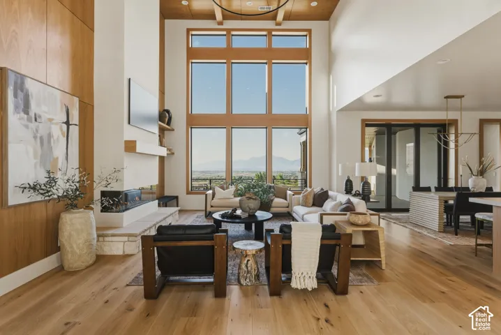 Two-story living area featuring extensive window walls, wood-finish flooring, a linear fireplace with stone hearth, a wood-paneled accent wall, and a wood-slat ceiling with exposed beams