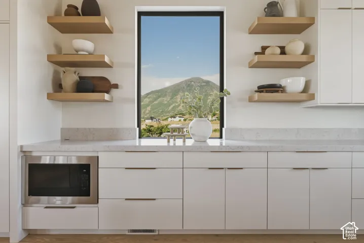 Modern kitchen cabinetry featuring a built-in microwave, light-toned countertops, and floating wood shelves