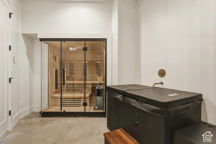 Glass-enclosed sauna featuring light wood paneling and bench seating along side of the cold plunge and full shower.