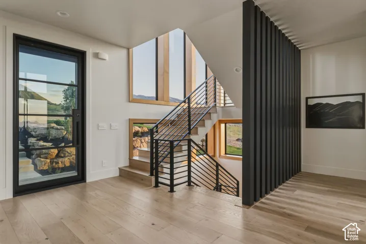 Contemporary entryway featuring a black-framed glass entry door, light wood-finish flooring, and a multi-level staircase with metal railings