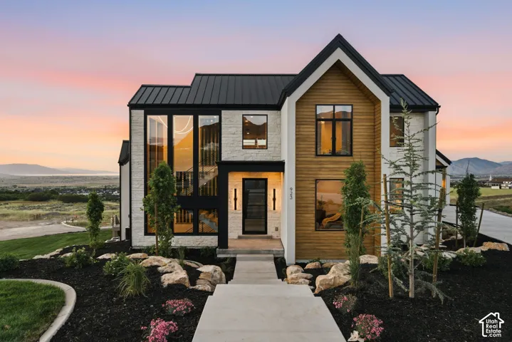 Contemporary exterior featuring a black metal roof, vertical wood-finish siding, light-colored stone veneer, and extensive black-framed windows