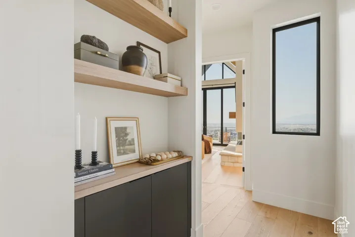 Open hallway with wood-finish flooring, a tall vertical window, and a built-in cabinet with floating shelves