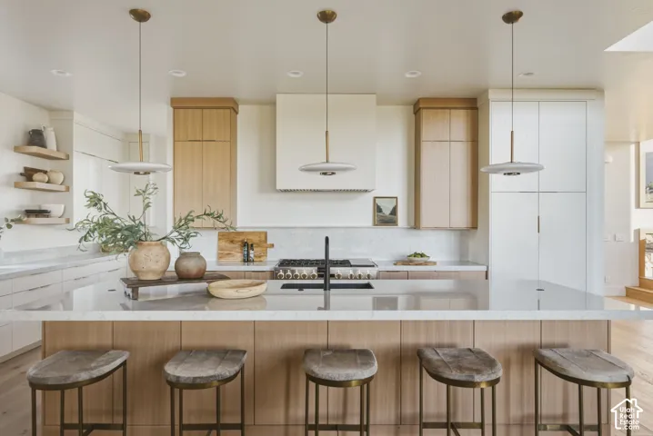 Spacious kitchen featuring a large island with seating, a gas range, integrated hood, and a combination of white and wood-finish cabinetry
