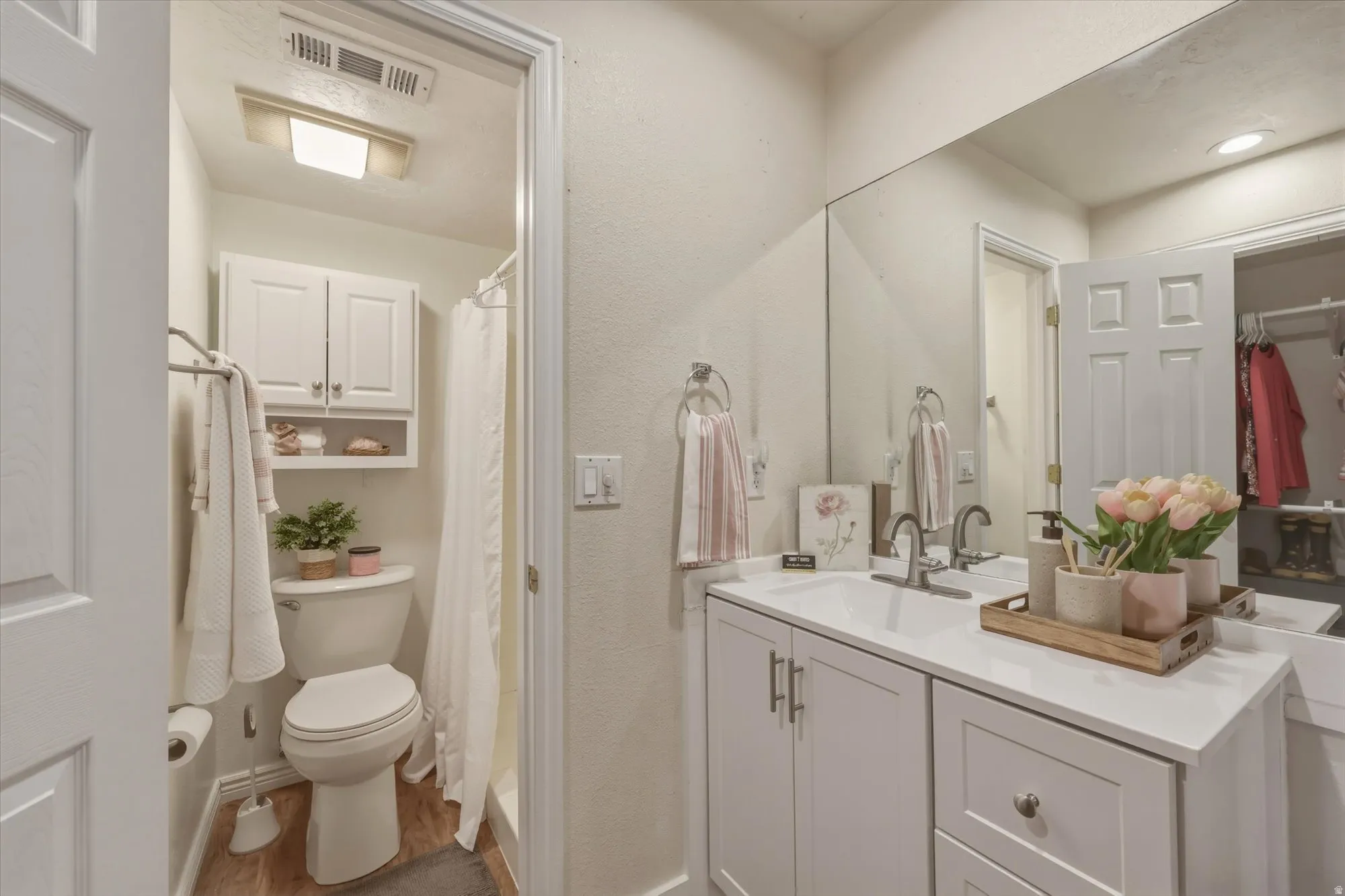 Bathroom featuring a white vanity with a single basin sink, light-toned countertop, and full-wall mirror