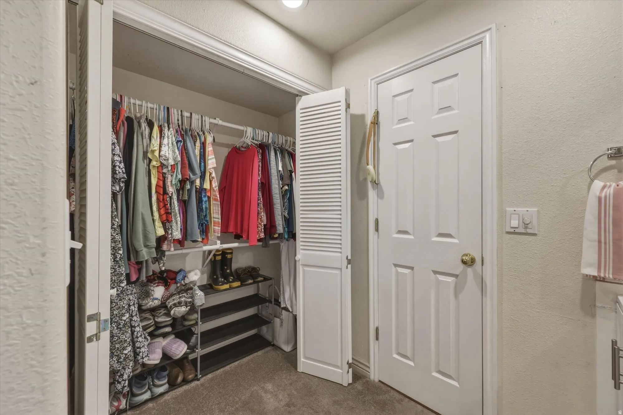 Bifold louvered closet doors opening to a carpeted interior with upper shelving and hanging rods