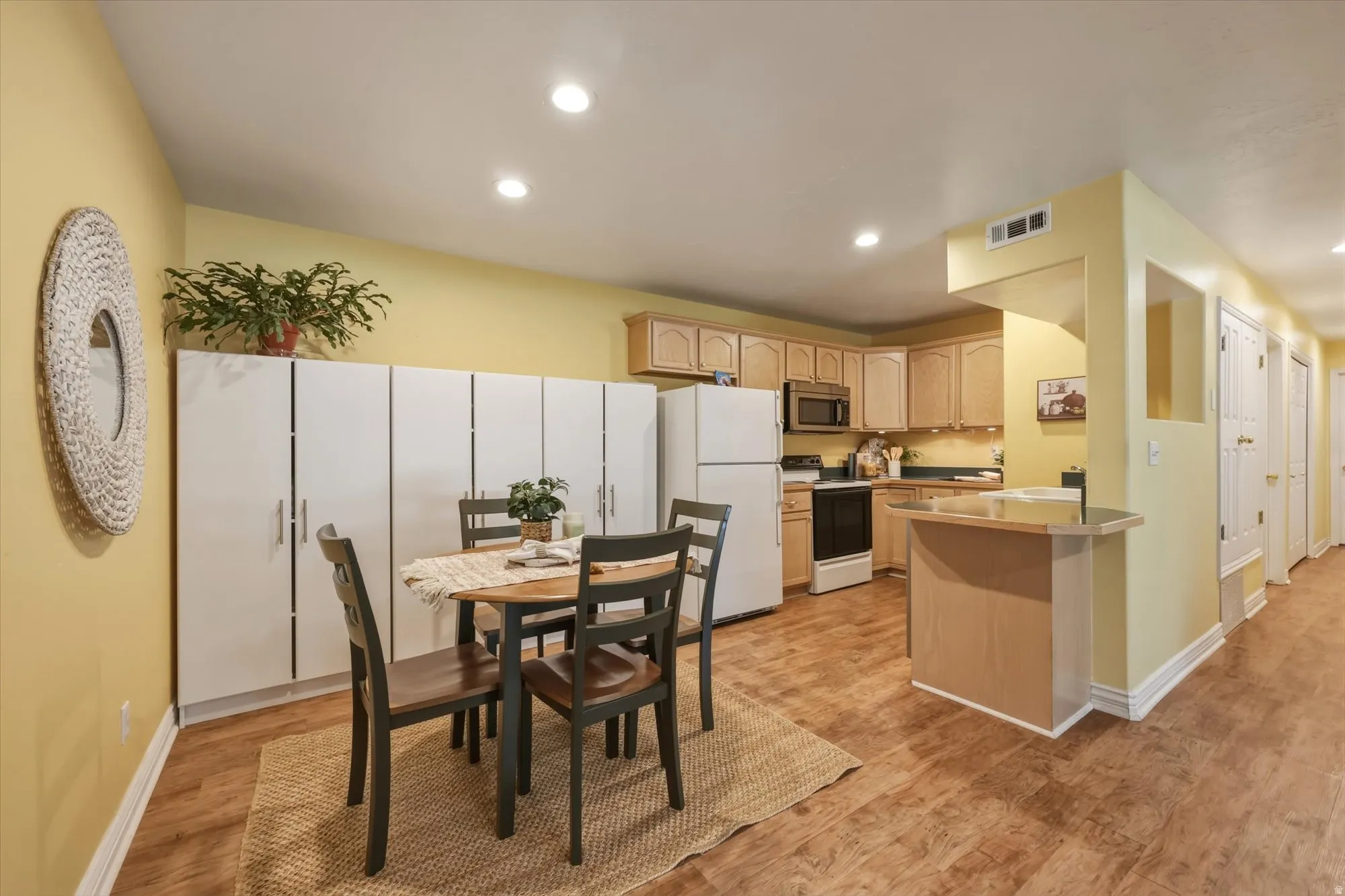 Kitchen and dining area featuring wood-finish flooring, recessed lighting, light wood cabinetry, white appliances, and a breakfast bar