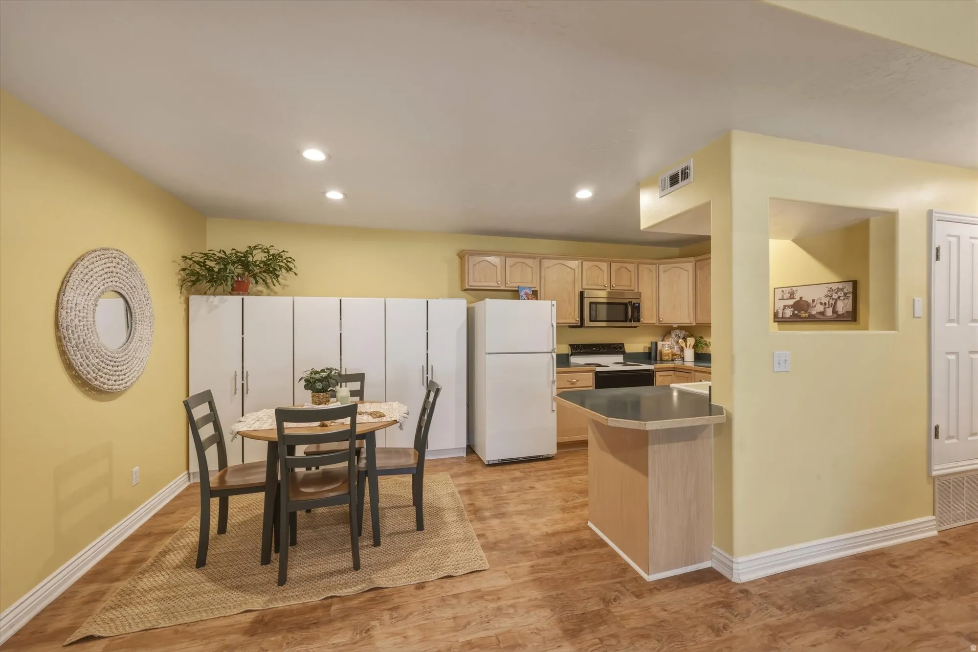 Wood-finish flooring throughout, featuring a kitchen with light wood cabinetry, a built-in microwave, and a breakfast bar