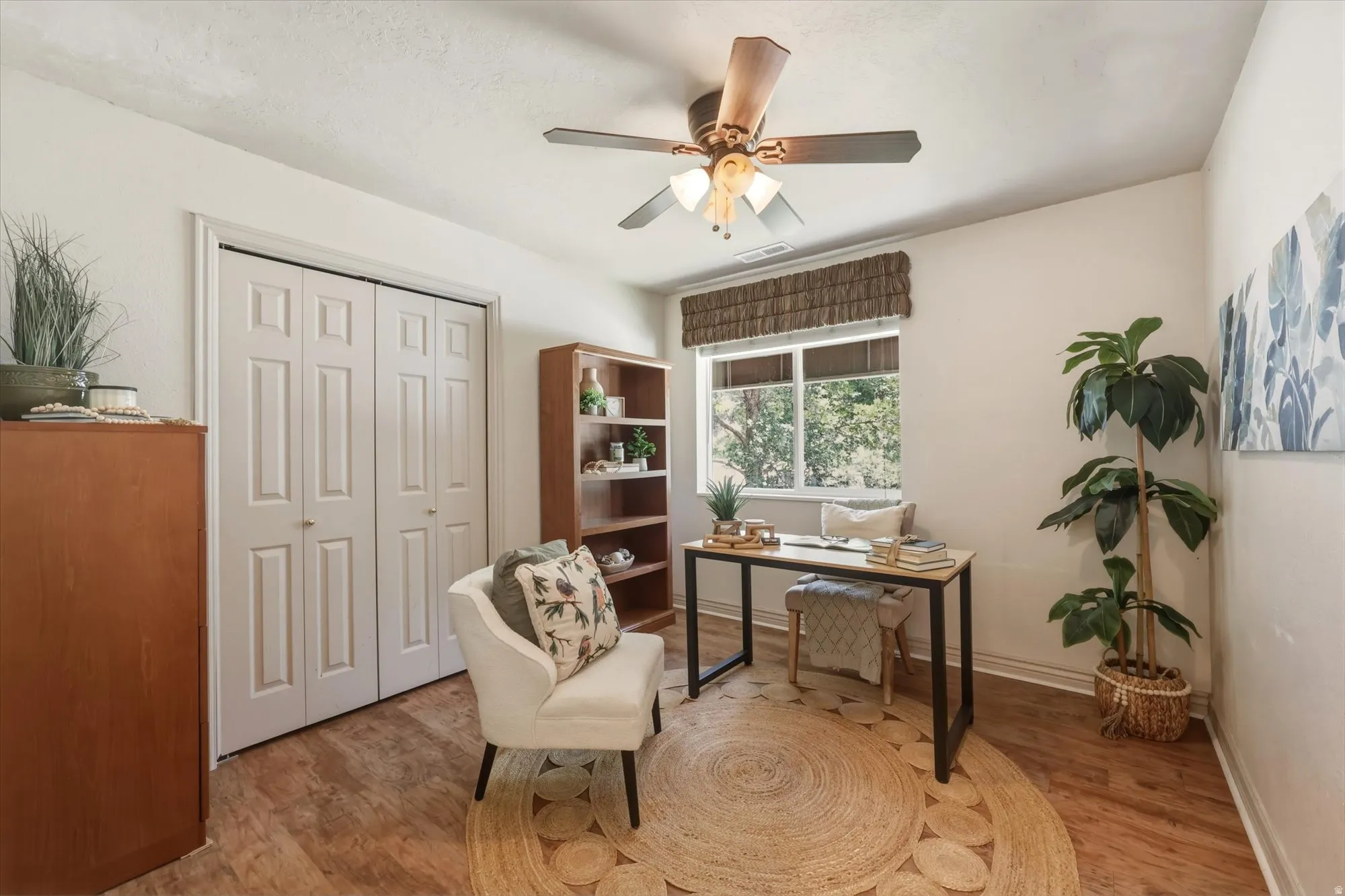 Room featuring wood-finish flooring, a window with a textured blind, and a ceiling fan with integrated lighting