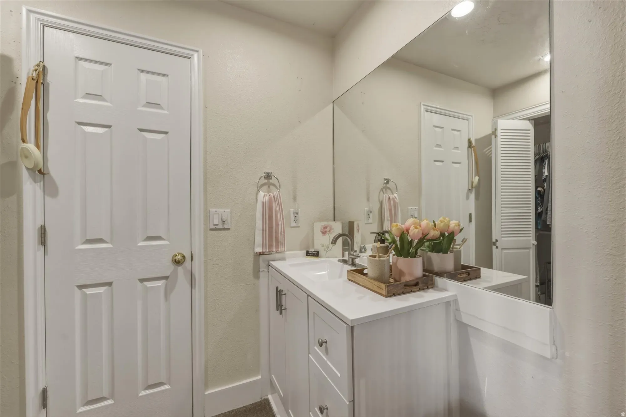 Bathroom vanity with white cabinetry, a single basin sink, and a white countertop