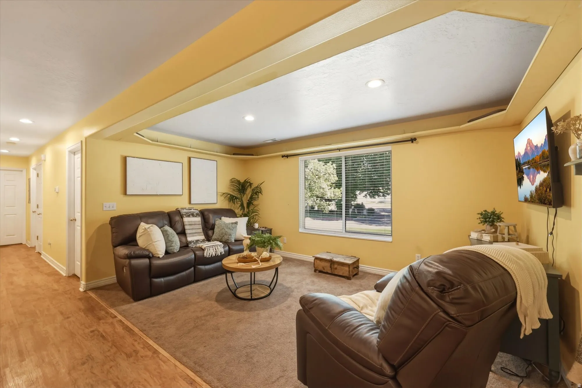 Spacious recreation area featuring recessed lighting, a large window with blinds, and a combination of wood-finish flooring and carpeting