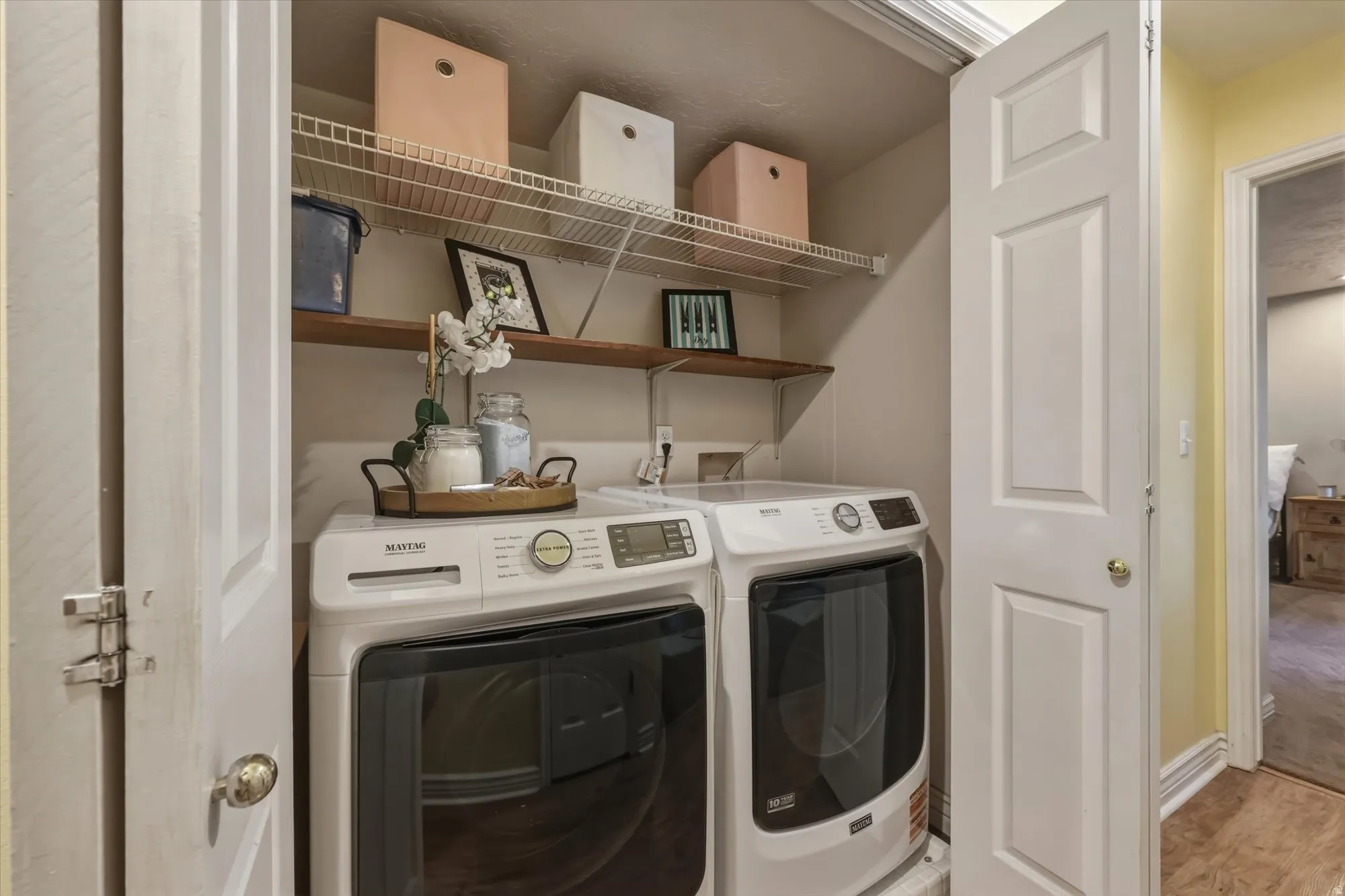 Dedicated laundry closet featuring a side-by-side washer and dryer set, wire shelving, and a wood-finish shelf