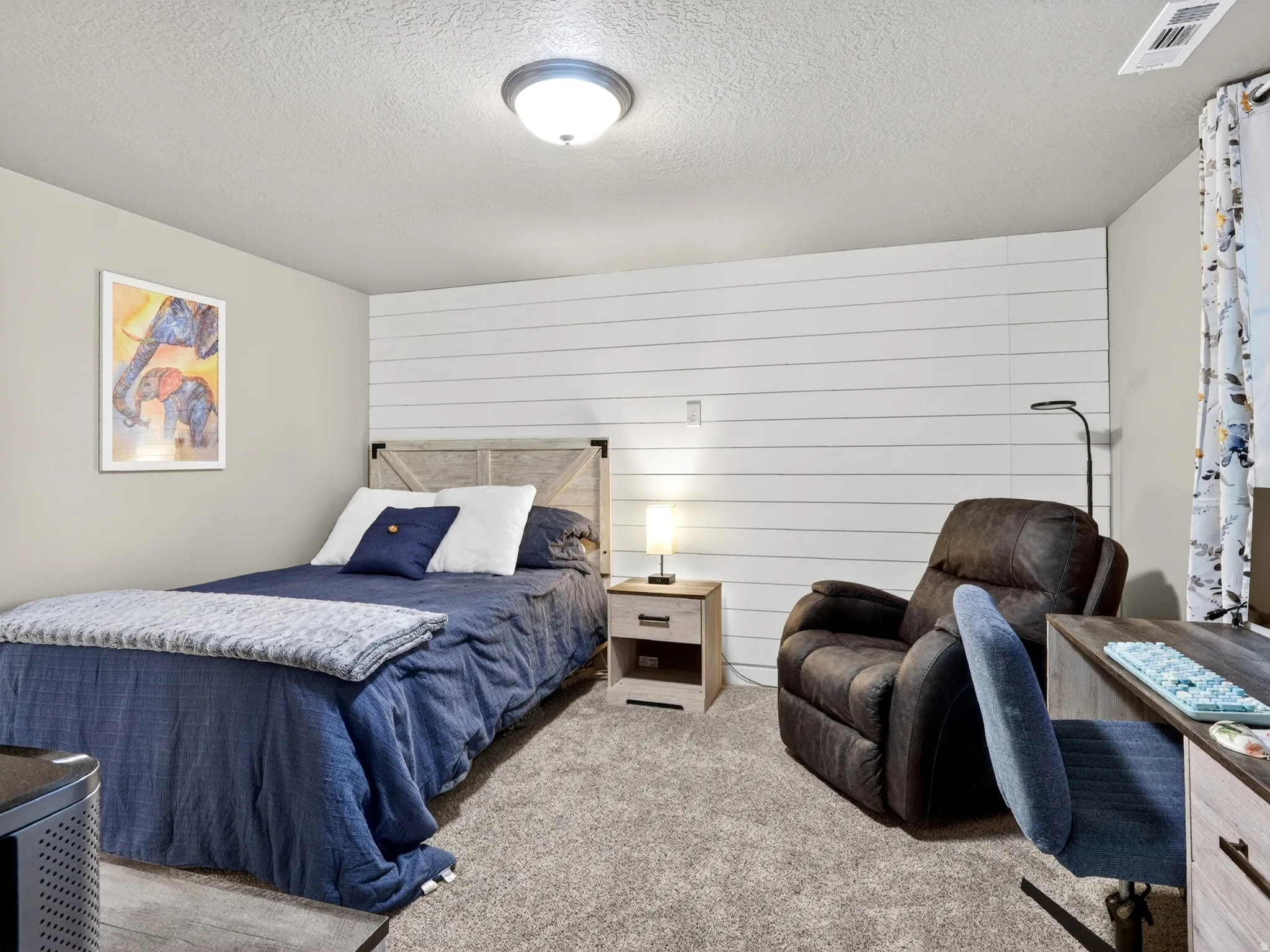 Wall-to-wall carpeting and a ceiling-mounted light fixture illuminate this room, featuring a shiplap accent wall