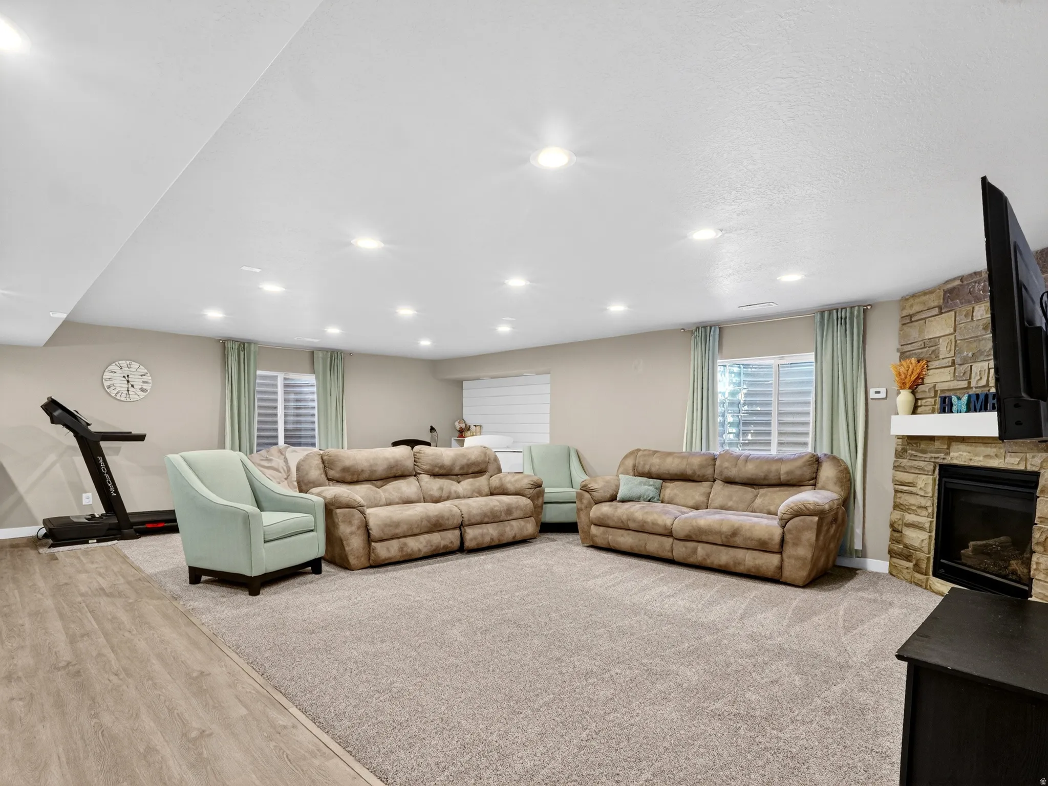 Spacious recreation room featuring recessed lighting, a stone-clad fireplace with a mantel, light wood-finish flooring, and soft carpet