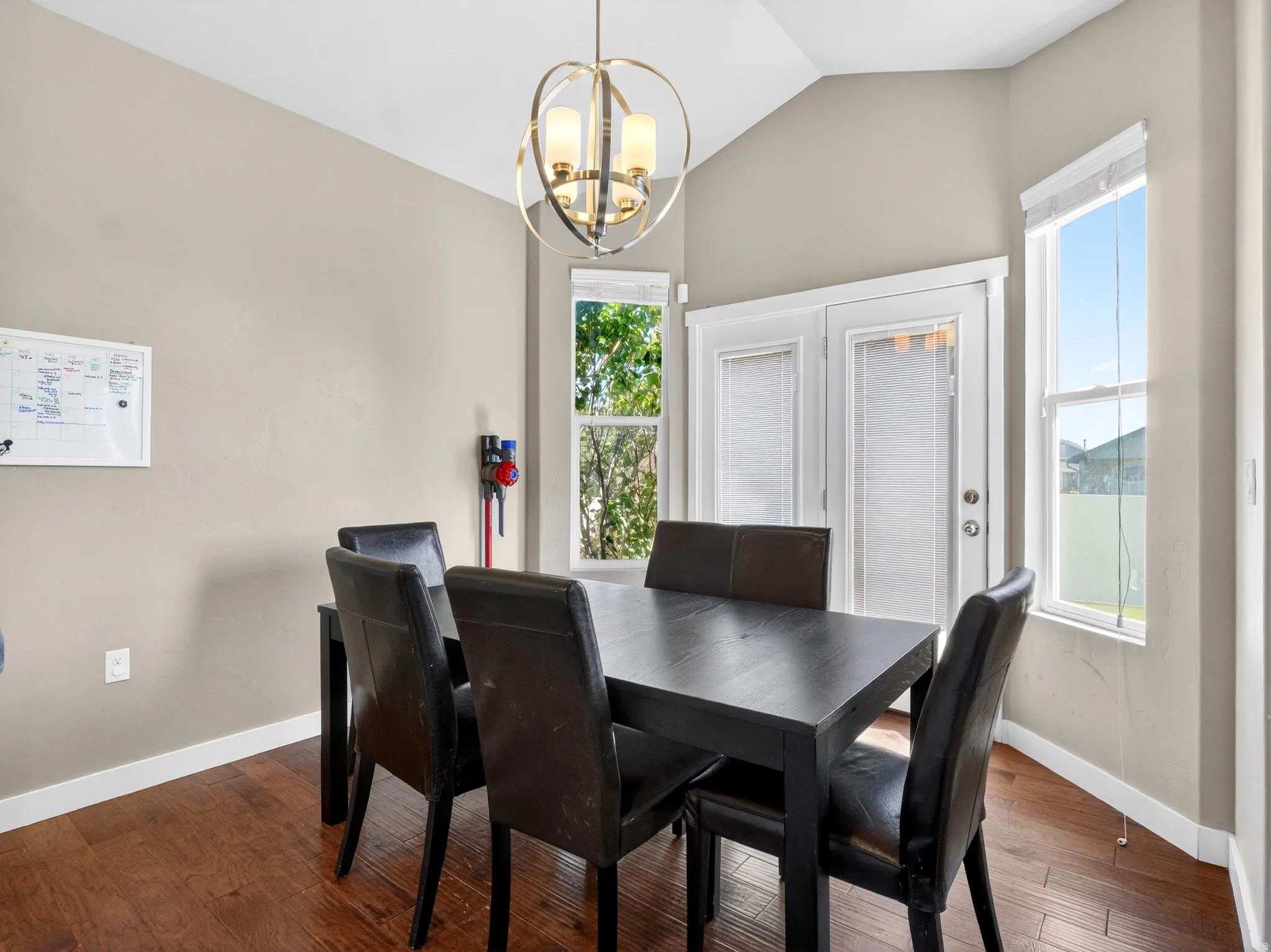 Formal dining space featuring a vaulted ceiling with a contemporary chandelier, rich wood-finish flooring, and light neutral wall tones