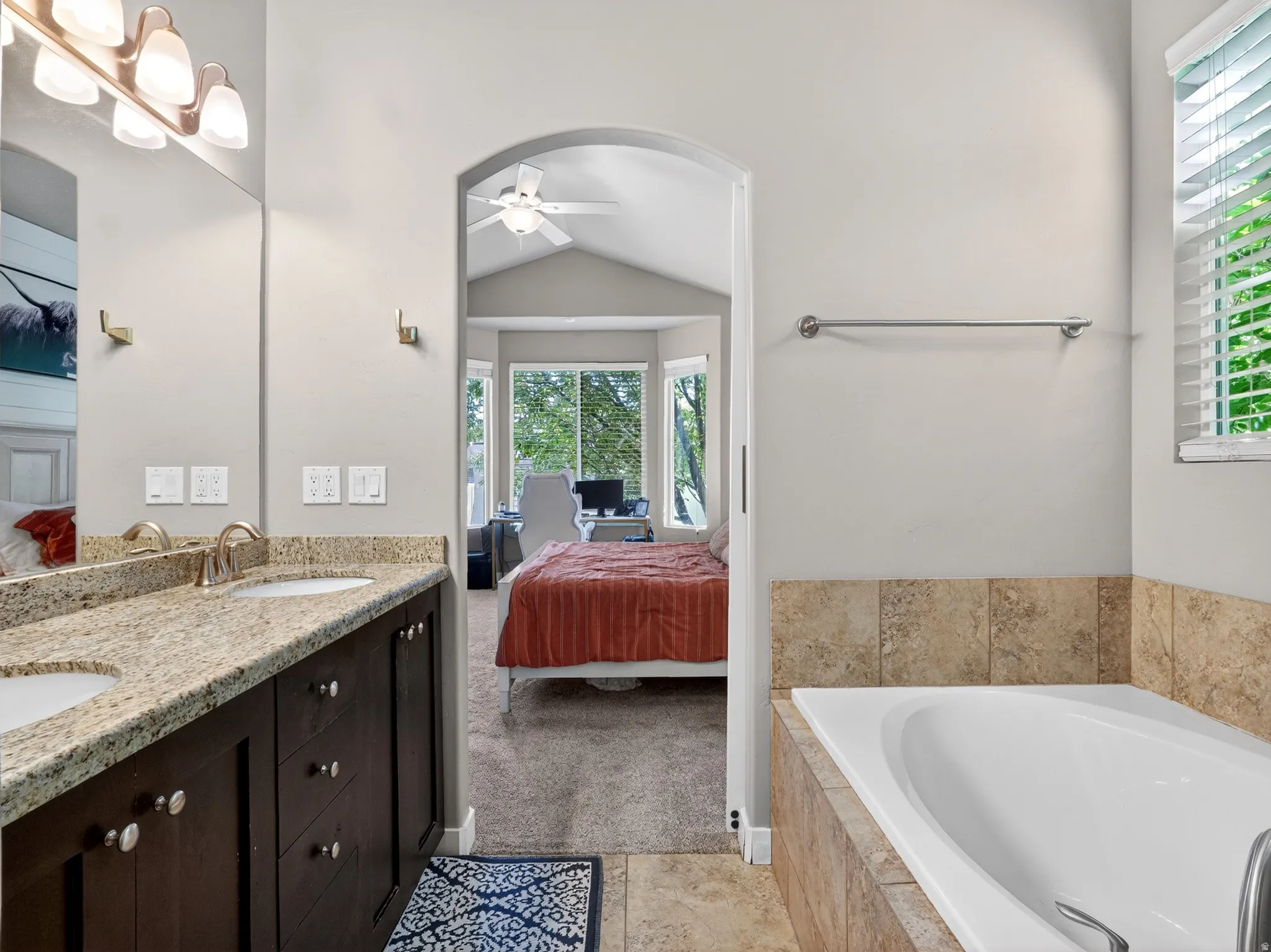 Bathroom featuring a built-in soaking tub with stone tile surround, a dual vanity with granite-style countertop, and dark wood cabinetry