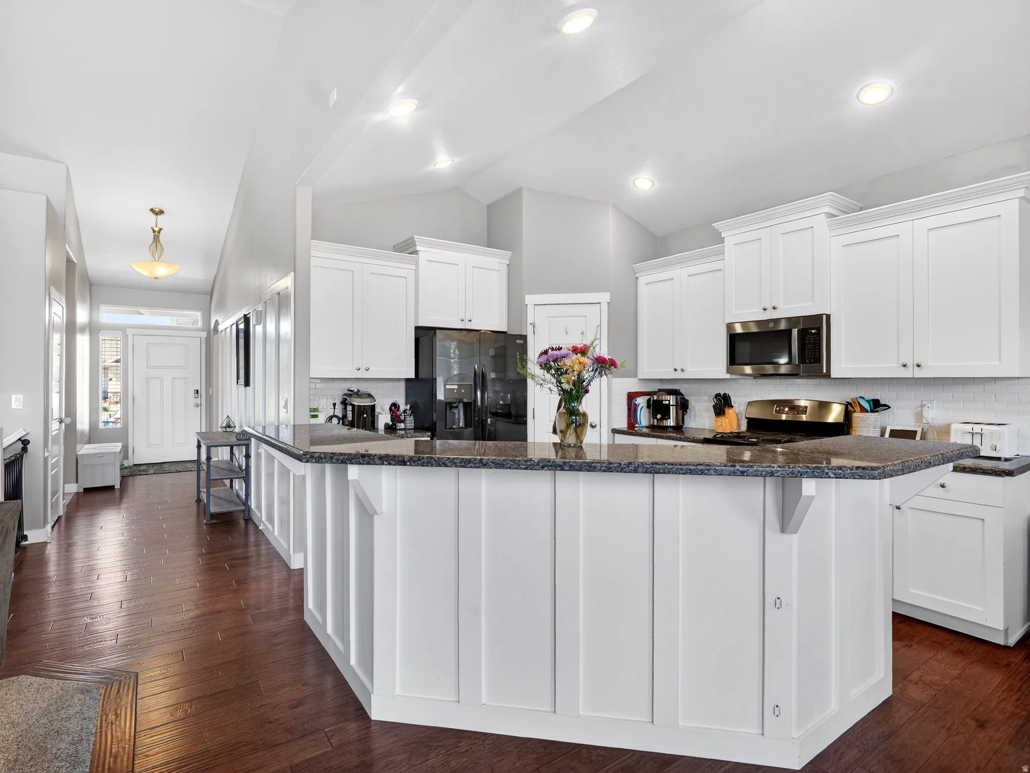 Open-concept kitchen featuring white shaker cabinetry, stainless steel appliances, a dark granite-finish countertop, and wood-finish flooring