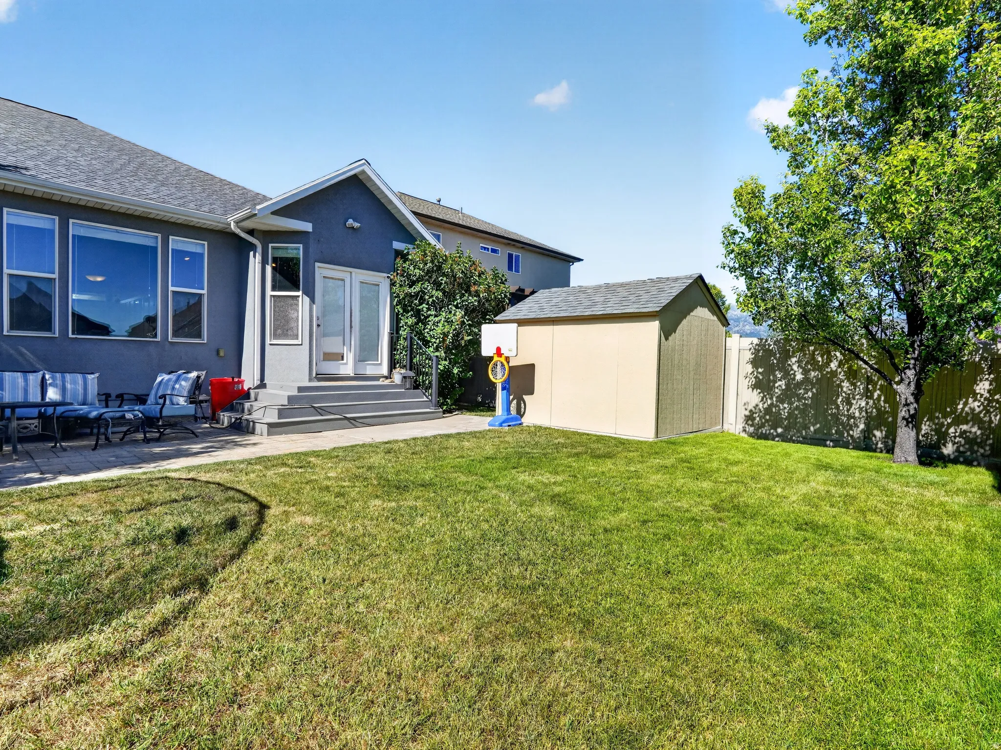 Expansive backyard featuring a lush lawn, a beige storage shed, and a mature tree