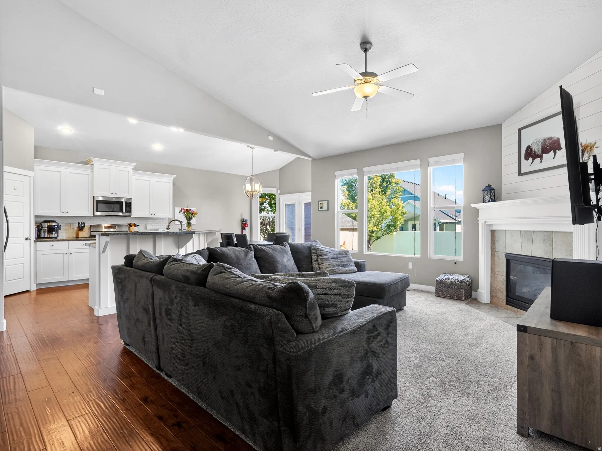 Open-concept living space featuring vaulted ceilings, a fireplace with a mantel, multiple large windows, and a ceiling fan