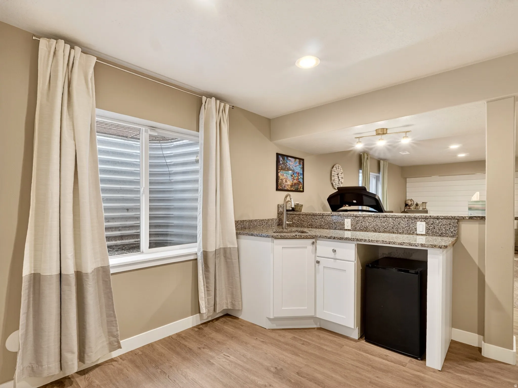 Wet bar featuring white cabinetry, granite countertops, an undermount sink with a gooseneck faucet, and a built-in beverage refrigerator