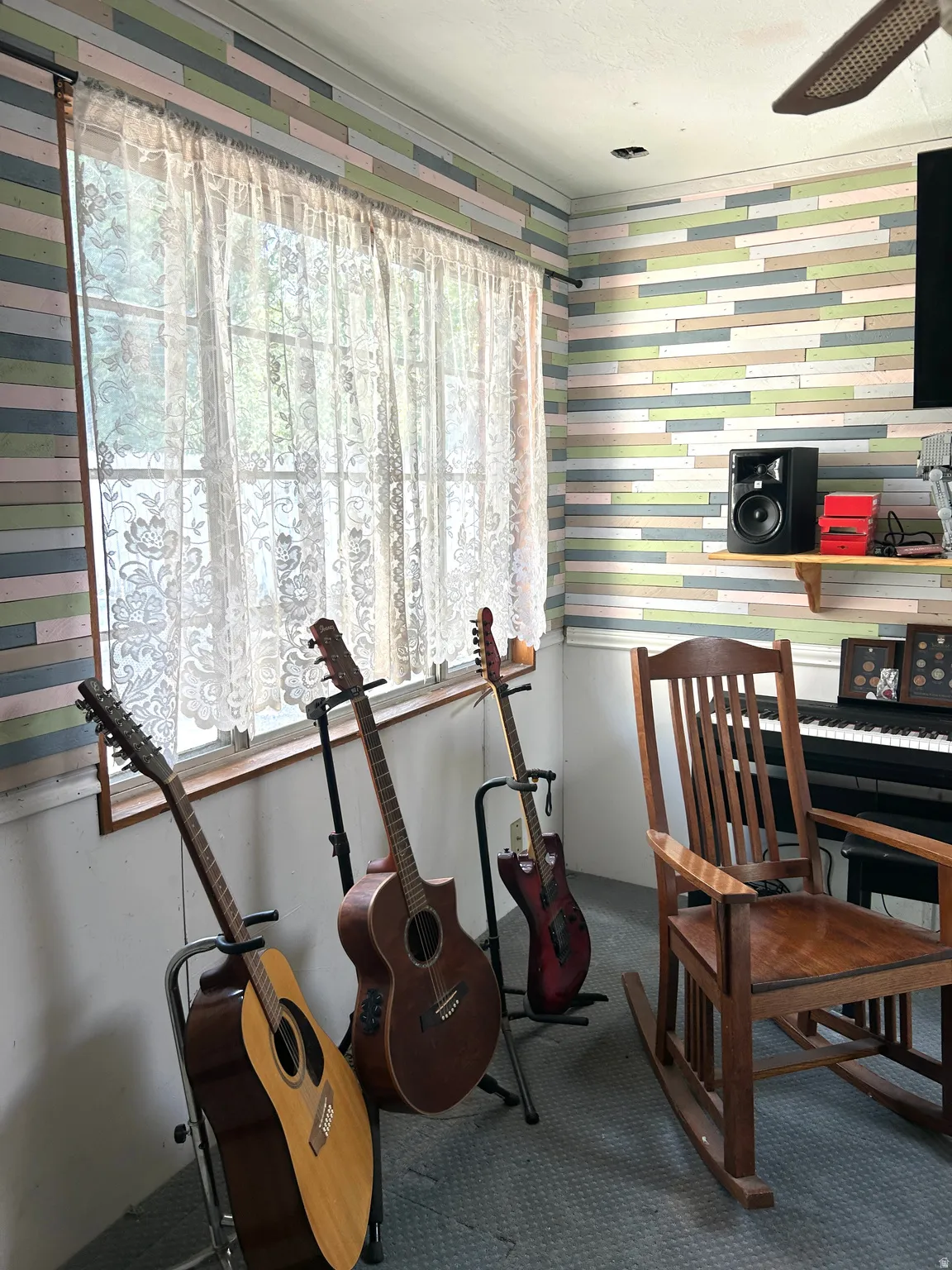 Room featuring a window with lace privacy curtains, colorful horizontal paneling, and a built-in shelf