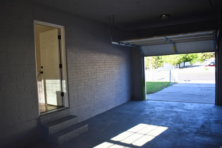 Attached garage with painted brick walls, concrete flooring, and an interior access door featuring two steps