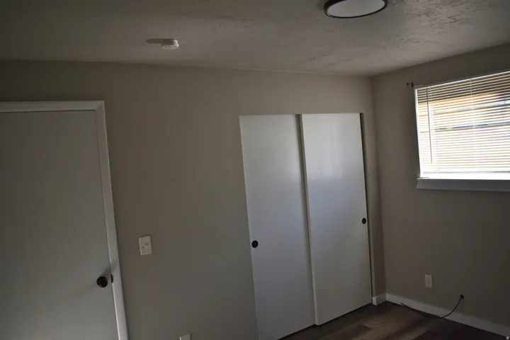 Interior room featuring a sliding double-door closet, a single window with blinds, and wood-finish flooring