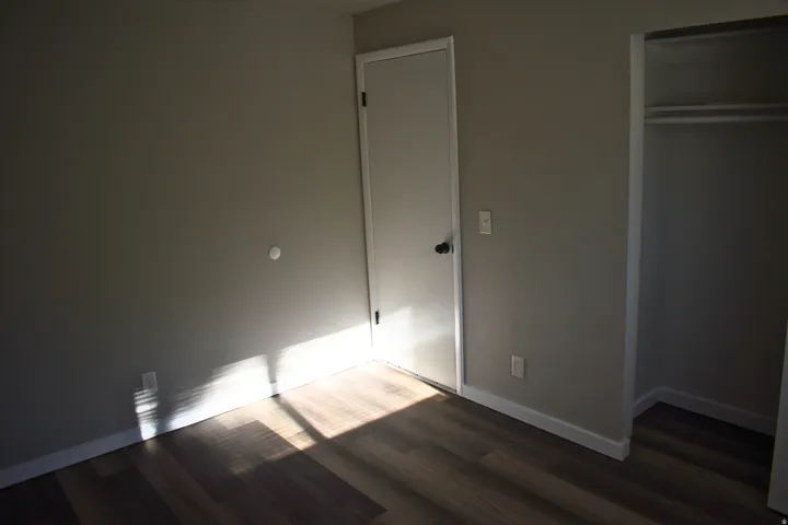 Neutral-toned walls complement wood-finish flooring in this room featuring a standard door and an open closet with shelving