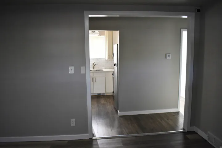 Kitchen entry featuring wood-finish flooring, white cabinetry, and a subway tile backsplash