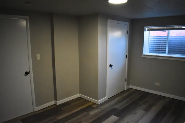 Room featuring wood-finish flooring, two white doors with matte black hardware, a flush-mount ceiling light fixture, and a window with a white frame