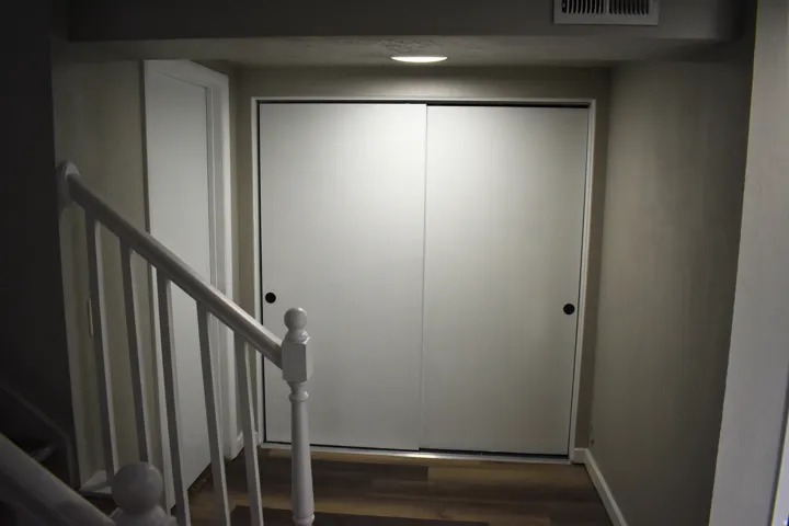 White sliding closet doors with black hardware, wood-finish flooring, and a white painted banister