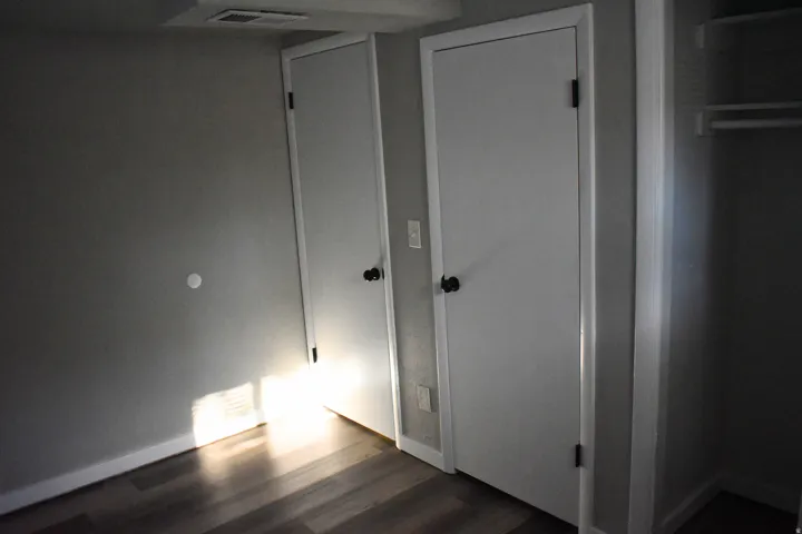 Two white doors with dark hardware, wood-finish flooring, and light grey painted walls