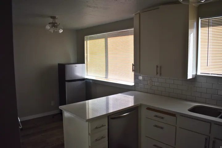 Kitchen featuring white cabinetry, subway tile backsplash, light-toned countertops, and wood-finish flooring