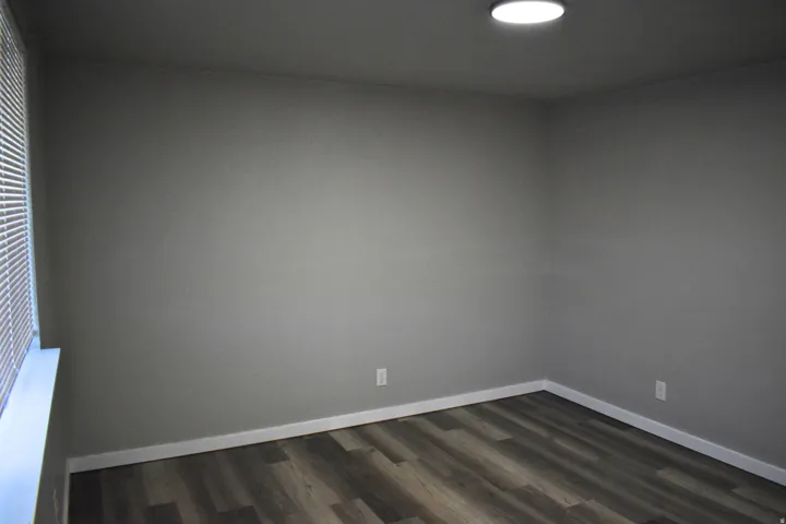 Room featuring neutral gray walls, wood-finish flooring, white baseboards, and a recessed ceiling light fixture