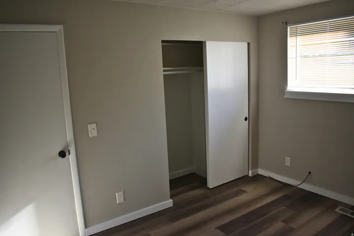 Room featuring wood-finish flooring, neutral wall tones, a window with horizontal blinds, a closet with sliding doors, and white baseboards