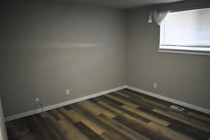 Room featuring wood-finish flooring, neutral wall tones, white trim, and a window with horizontal blinds