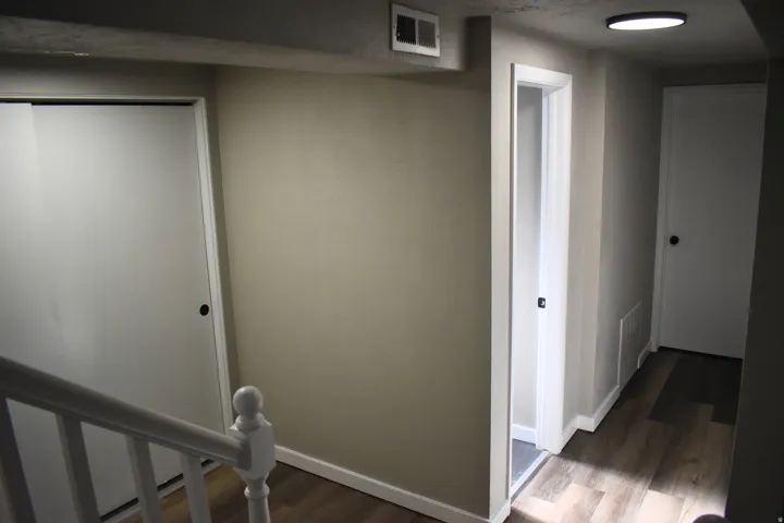 Corridor featuring wood-finish flooring, white baseboards, a white staircase with a baluster newel post, and flush-mount lighting