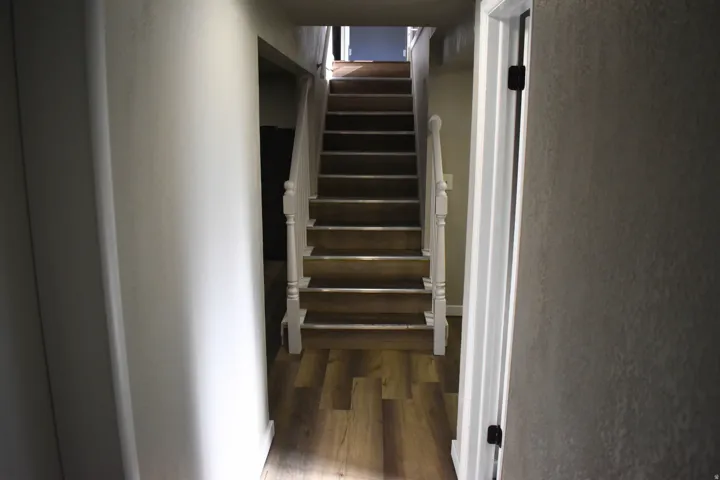Staircase featuring wood-finish treads and risers, white painted balusters and newel posts, and a handrail