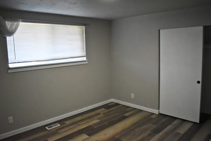 Room featuring wood-finish flooring, neutral wall paint, white baseboards, and a window with blinds