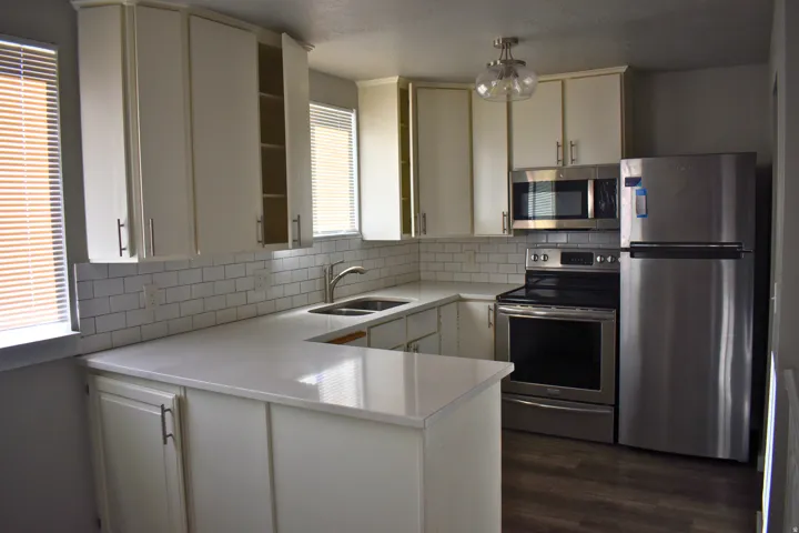 Kitchen featuring white cabinetry, light countertops, stainless steel appliances, white subway tile backsplash, and wood-finish flooring