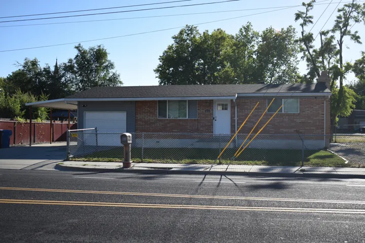 Brick exterior home featuring a chain-link fence, attached garage, and covered carport