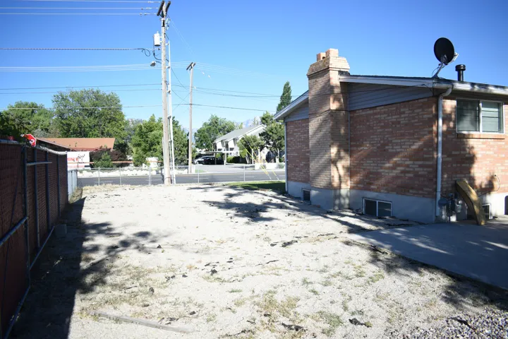 Expansive side yard featuring a chain-link fence, a paved section, and a brick exterior with a chimney