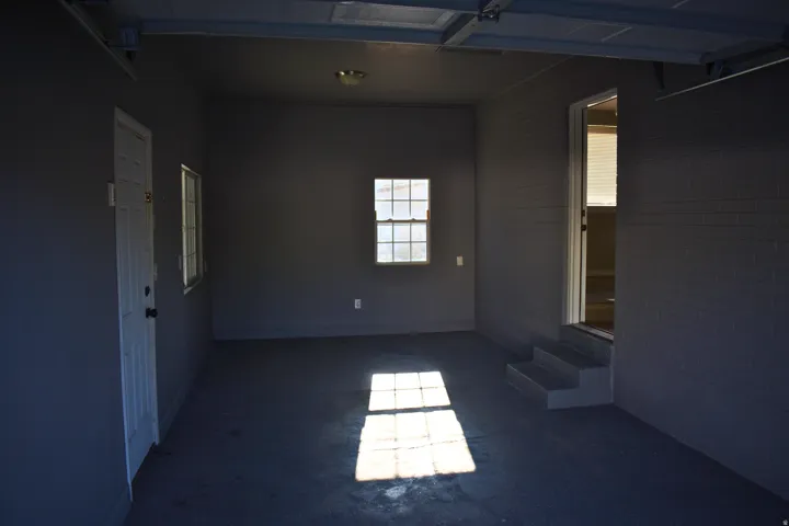 Spacious garage featuring painted concrete flooring, a side entry door, two windows providing natural light, and a dedicated entry with steps into the interior space
