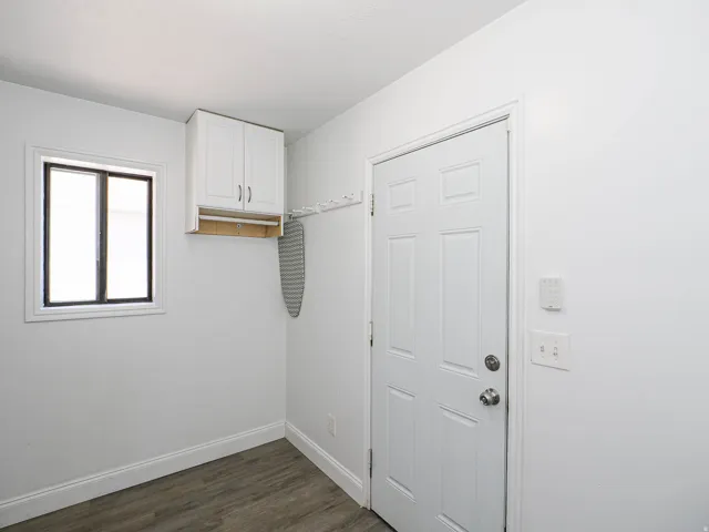 Utility space featuring wood-finish flooring, a white paneled door, and a built-in white cabinet