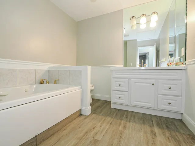 Bathroom featuring a built-in soaking tub with brass fixtures, a white vanity with a light-colored countertop, and a large wall-mounted mirror