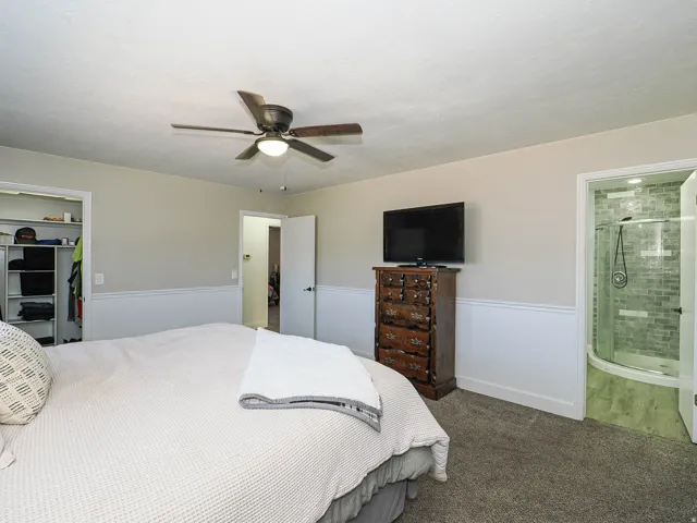 Carpeted bedroom featuring a ceiling fan with integrated lighting, wainscoting, and an open closet with built-in shelving
