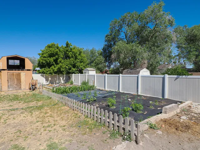 Backyard featuring a garden plot with a picket fence, a light-toned privacy fence, a two-story shed, and an additional storage shed