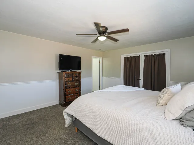 Carpeted room featuring a ceiling fan with integrated lighting, two-tone painted walls with wainscoting, and white trim
