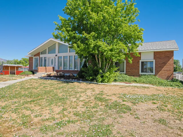 Brick exterior featuring an A-frame architectural style, a white front entry door, a series of tall vertical windows, a substantial mature tree, and a rock-lined planting bed