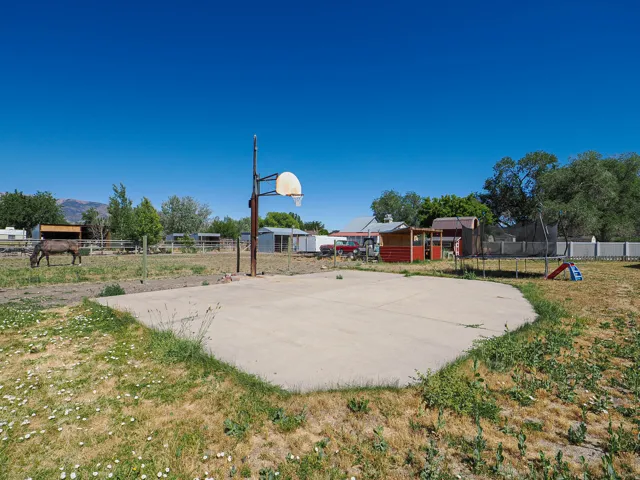 Expansive concrete basketball court with hoop, surrounded by fencing and open land