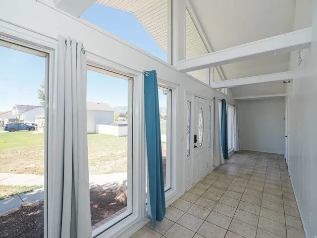 Entryway featuring an architectural vaulted ceiling with exposed beams, full-height windows, a paneled entry door with decorative glass inserts, and ceramic tile flooring